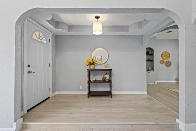 entryway with a raised ceiling, visible vents, arched walkways, light wood-style floors, and baseboards