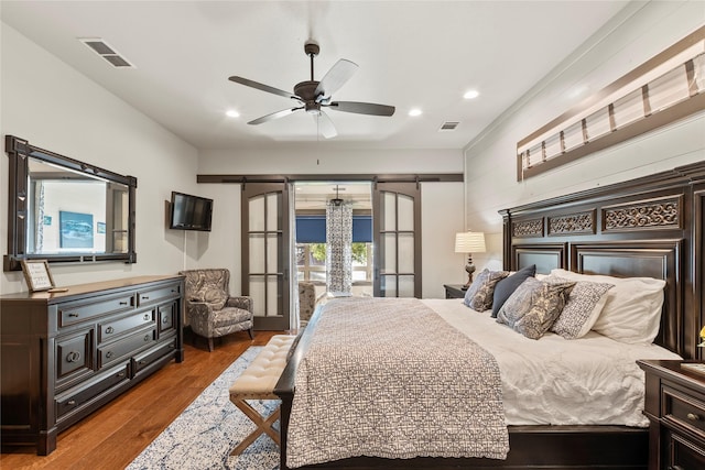 bedroom with a barn door, wood finished floors, visible vents, and recessed lighting