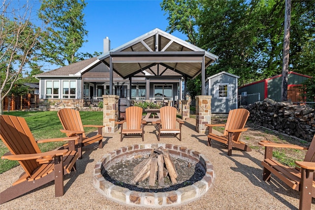 rear view of property with a chimney, a shed, an outbuilding, stone siding, and an outdoor fire pit