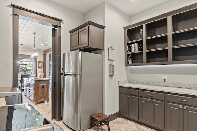kitchen featuring baseboards, freestanding refrigerator, light stone counters, and gray cabinets