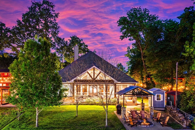 back of house at dusk with a chimney, an outdoor structure, a yard, a shed, and an outdoor fire pit