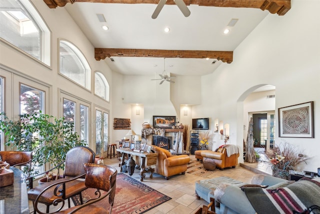 living room featuring beamed ceiling, arched walkways, ceiling fan, and a towering ceiling