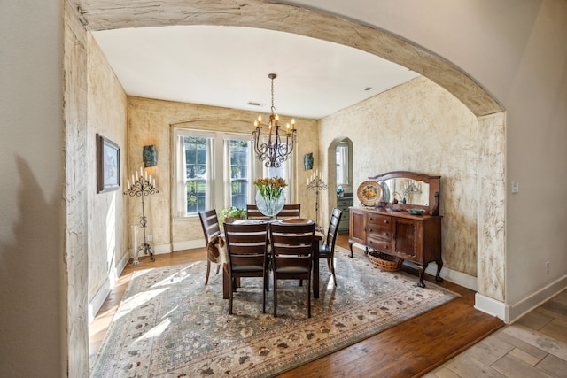 dining room with visible vents, wood finished floors, baseboards, a chandelier, and arched walkways