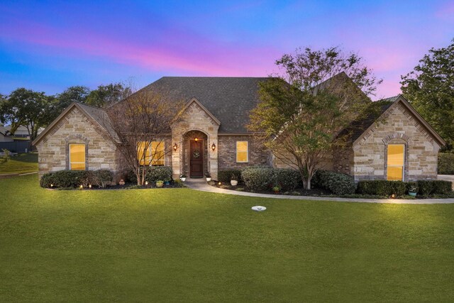 french country inspired facade with a lawn and stone siding