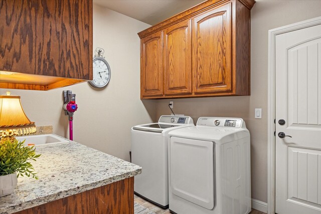 laundry area featuring cabinet space, washing machine and dryer, a sink, and light wood-style floors