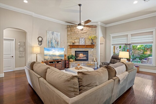 living room featuring arched walkways, ceiling fan, ornamental molding, and a stone fireplace