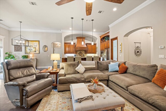 living room featuring visible vents, arched walkways, ceiling fan with notable chandelier, and ornamental molding