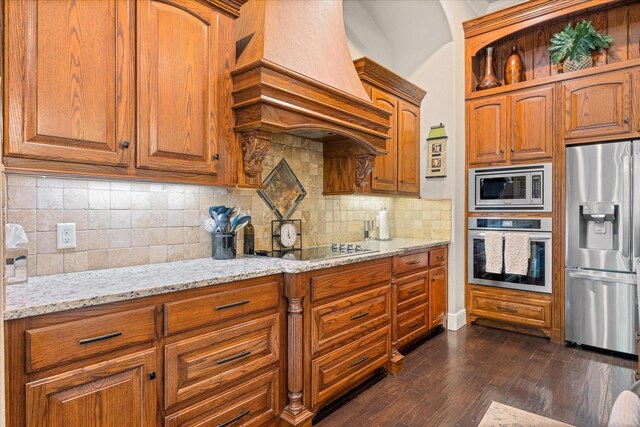 kitchen with stainless steel appliances, brown cabinetry, light stone counters, and custom exhaust hood