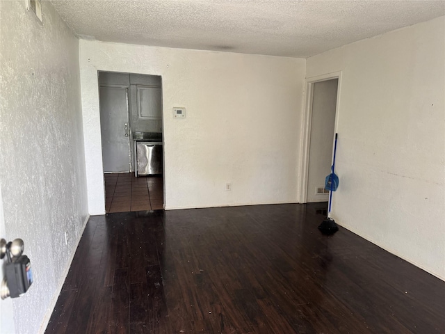 spare room featuring wood-type flooring, a textured wall, a textured ceiling, and visible vents