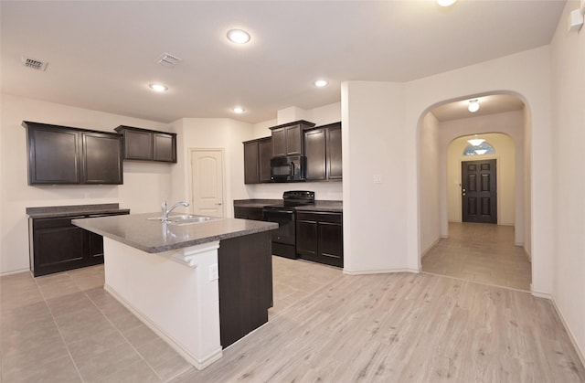 kitchen with visible vents, arched walkways, baseboards, a kitchen island with sink, and black appliances