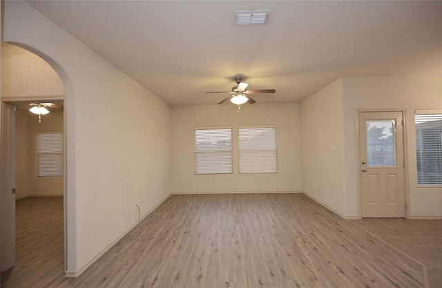 unfurnished room with visible vents, arched walkways, light wood-style floors, and ceiling fan