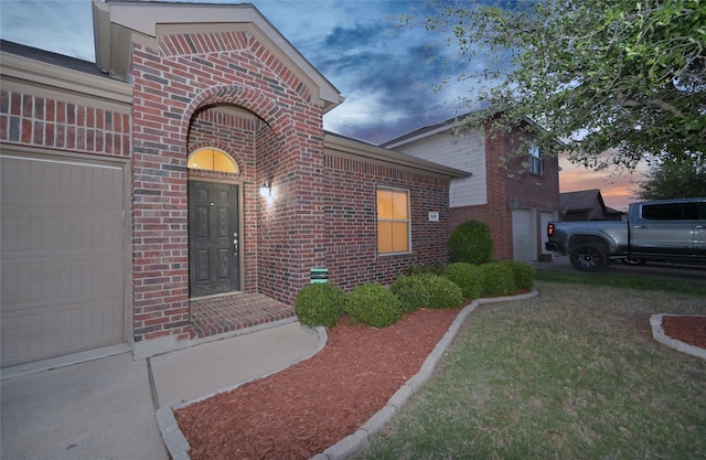 exterior entry at dusk with an attached garage and brick siding
