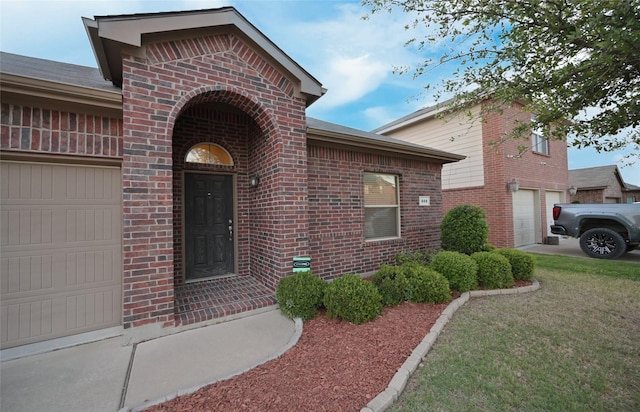 entrance to property with an attached garage, brick siding, and a yard