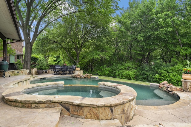 view of pool featuring grilling area, a patio area, outdoor dining space, and a pool with connected hot tub