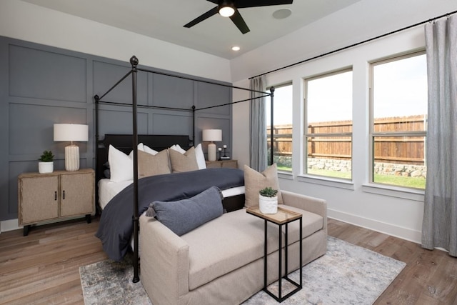 bedroom featuring light wood finished floors, ceiling fan, a decorative wall, and baseboards