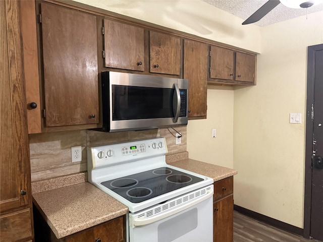 kitchen with white electric stove, stainless steel microwave, dark wood finished floors, ceiling fan, and light countertops