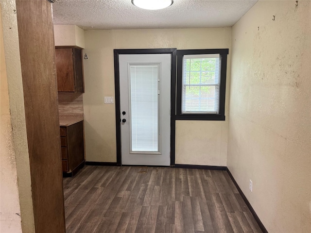 doorway with dark wood-type flooring, a textured ceiling, and baseboards
