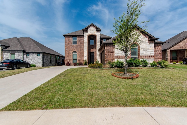 french country style house with stone siding, a front lawn, brick siding, and concrete driveway