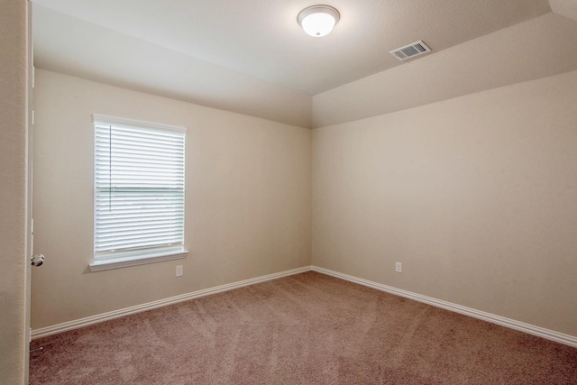 carpeted spare room with visible vents, vaulted ceiling, and baseboards