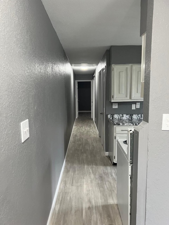 hall with a textured wall, baseboards, and wood finished floors
