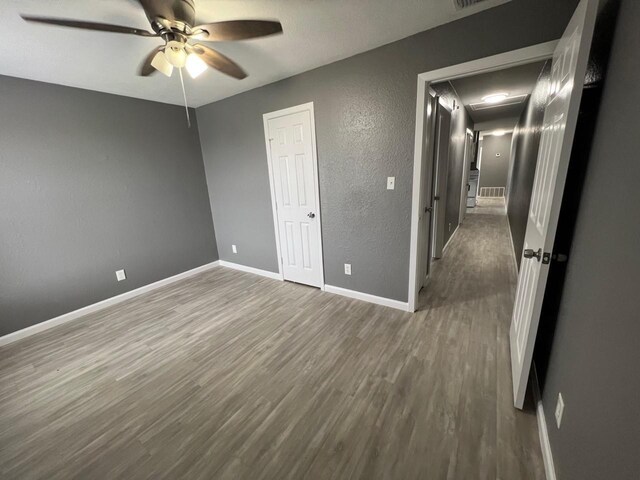 unfurnished bedroom with attic access, baseboards, ceiling fan, a textured wall, and dark wood-type flooring