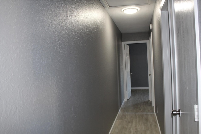 hallway featuring attic access, baseboards, and wood finished floors