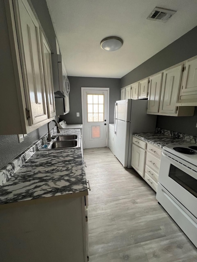 kitchen featuring light wood-style flooring, a sink, dark countertops, visible vents, and white appliances