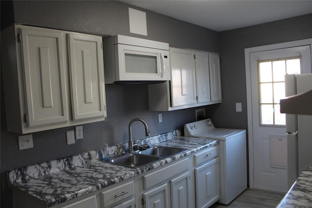 kitchen with white cabinets, wood finished floors, a sink, washer / dryer, and white microwave