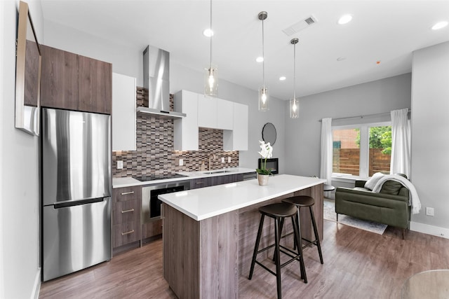 kitchen with wall chimney range hood, visible vents, modern cabinets, a sink, and freestanding refrigerator