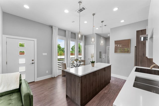 kitchen with visible vents, dark brown cabinetry, a kitchen island, light countertops, and a sink