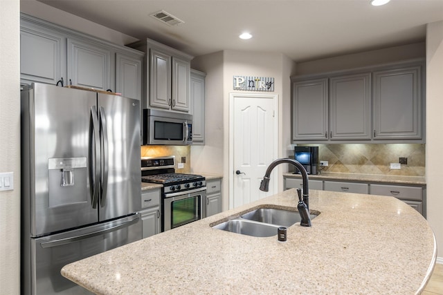 kitchen with a sink, a center island with sink, visible vents, gray cabinetry, and appliances with stainless steel finishes