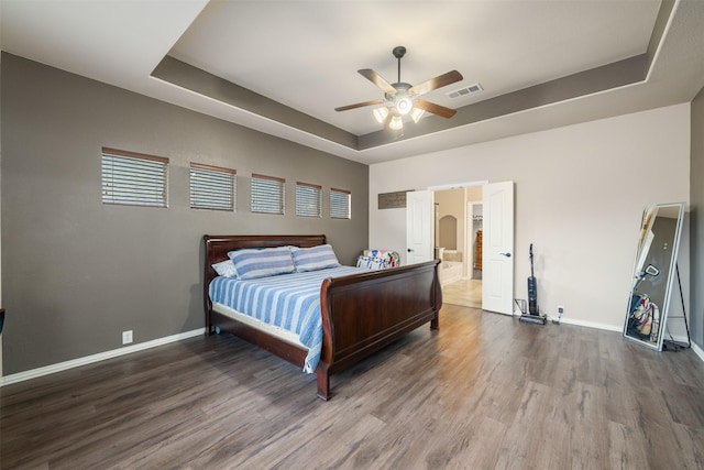 bedroom with a tray ceiling, visible vents, baseboards, a ceiling fan, and wood finished floors