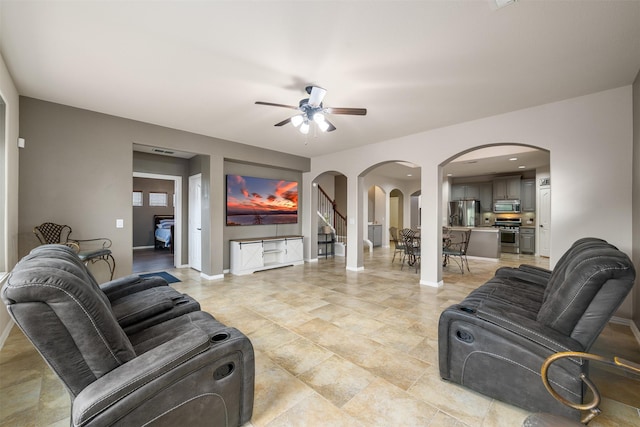 living room featuring arched walkways, a ceiling fan, and baseboards