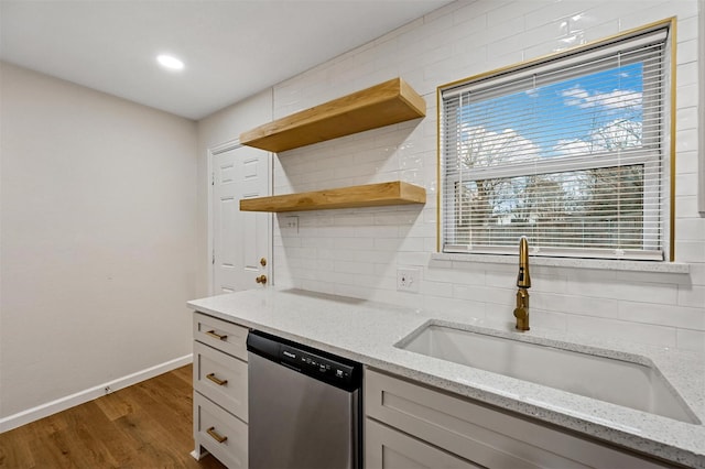 kitchen with open shelves, backsplash, wood finished floors, stainless steel dishwasher, and a sink