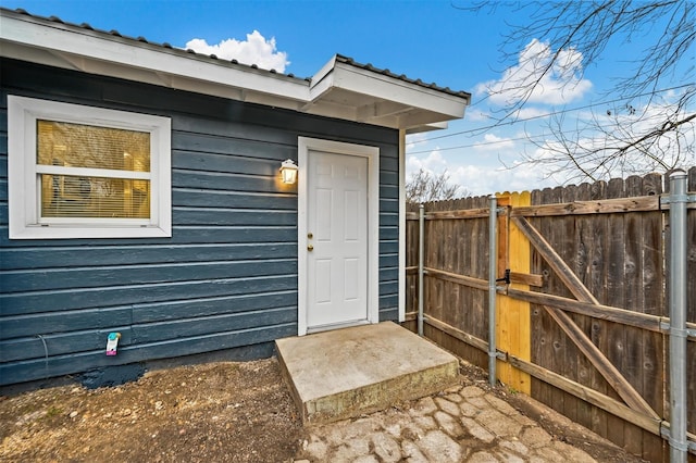 doorway to property with a gate, fence, and metal roof
