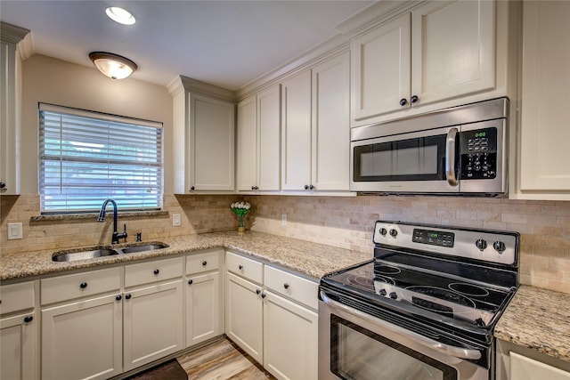 kitchen featuring a sink, white cabinetry, backsplash, light stone counters, and appliances with stainless steel finishes