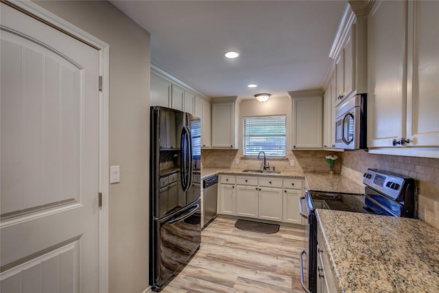 kitchen featuring a sink, decorative backsplash, light wood-type flooring, appliances with stainless steel finishes, and light stone countertops