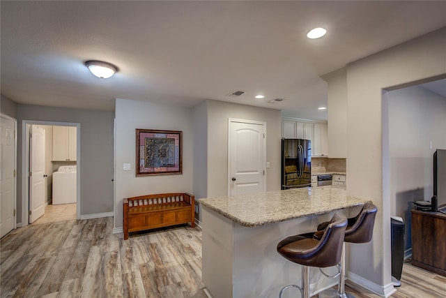 kitchen featuring freestanding refrigerator, light stone countertops, baseboards, a peninsula, and washer / clothes dryer
