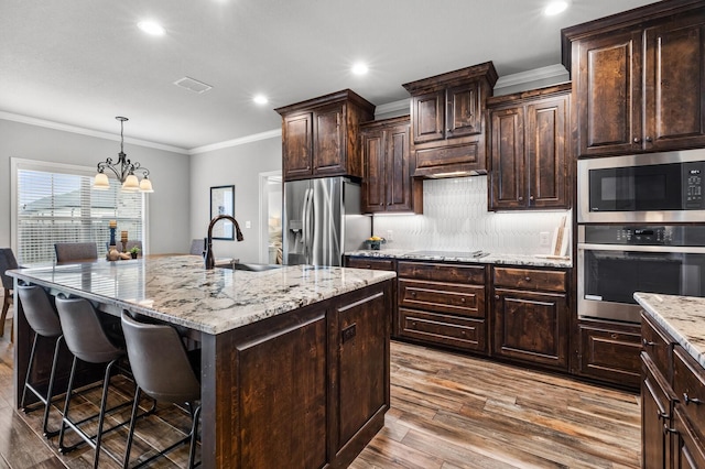 10009 Wildberry Dr, Waco, TX 76712 - kitchen featuring a sink, stainless steel appliances, wood finished floors, a breakfast bar area, and a center island with sink