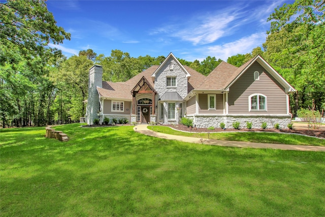craftsman-style home featuring a chimney, roof with shingles, stone siding, and a front yard