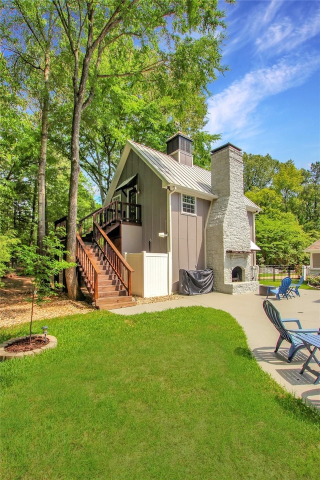 rear view of house with a chimney, an outdoor stone fireplace, a patio area, a lawn, and stairs