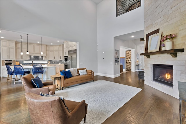 living room featuring recessed lighting, a stone fireplace, dark wood-type flooring, and baseboards