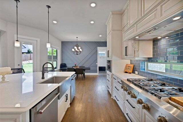 kitchen with a sink, appliances with stainless steel finishes, light countertops, custom range hood, and a notable chandelier
