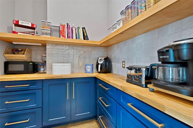 interior space featuring backsplash, butcher block counters, black microwave, and blue cabinets