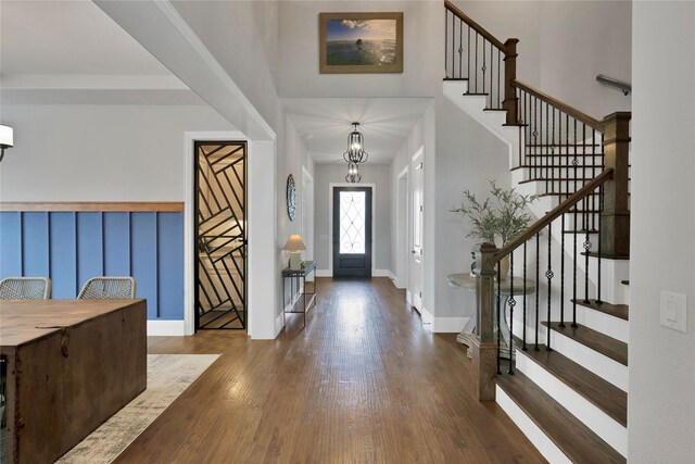foyer entrance with a towering ceiling, wood finished floors, baseboards, a chandelier, and stairs