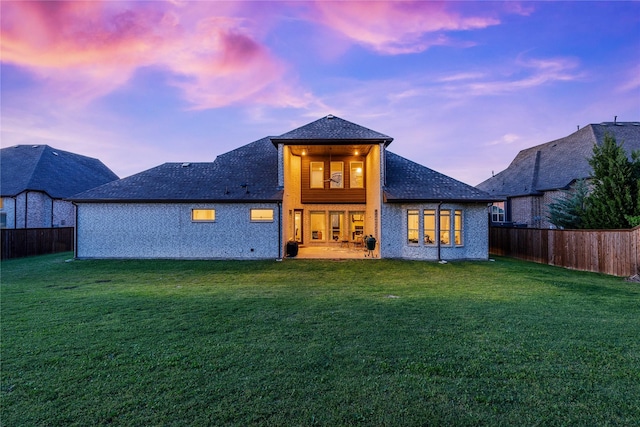back of property at dusk featuring a lawn and a fenced backyard