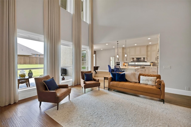 living room with recessed lighting, wood finished floors, a towering ceiling, and baseboards