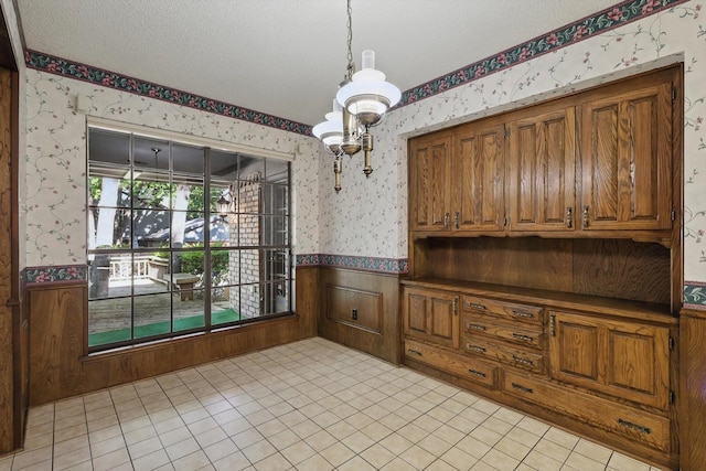 5112 River Ridge Rd, Arlington, TX 76017 - unfurnished dining area featuring wallpapered walls, wainscoting, a chandelier, a textured ceiling, and light tile patterned floors