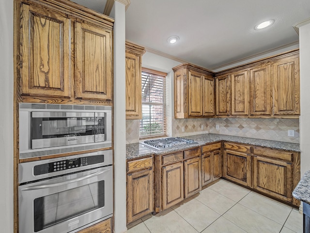 kitchen featuring backsplash, brown cabinetry, stainless steel appliances, and light tile patterned floors