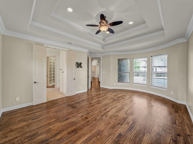 empty room with a raised ceiling, wood finished floors, baseboards, and ceiling fan
